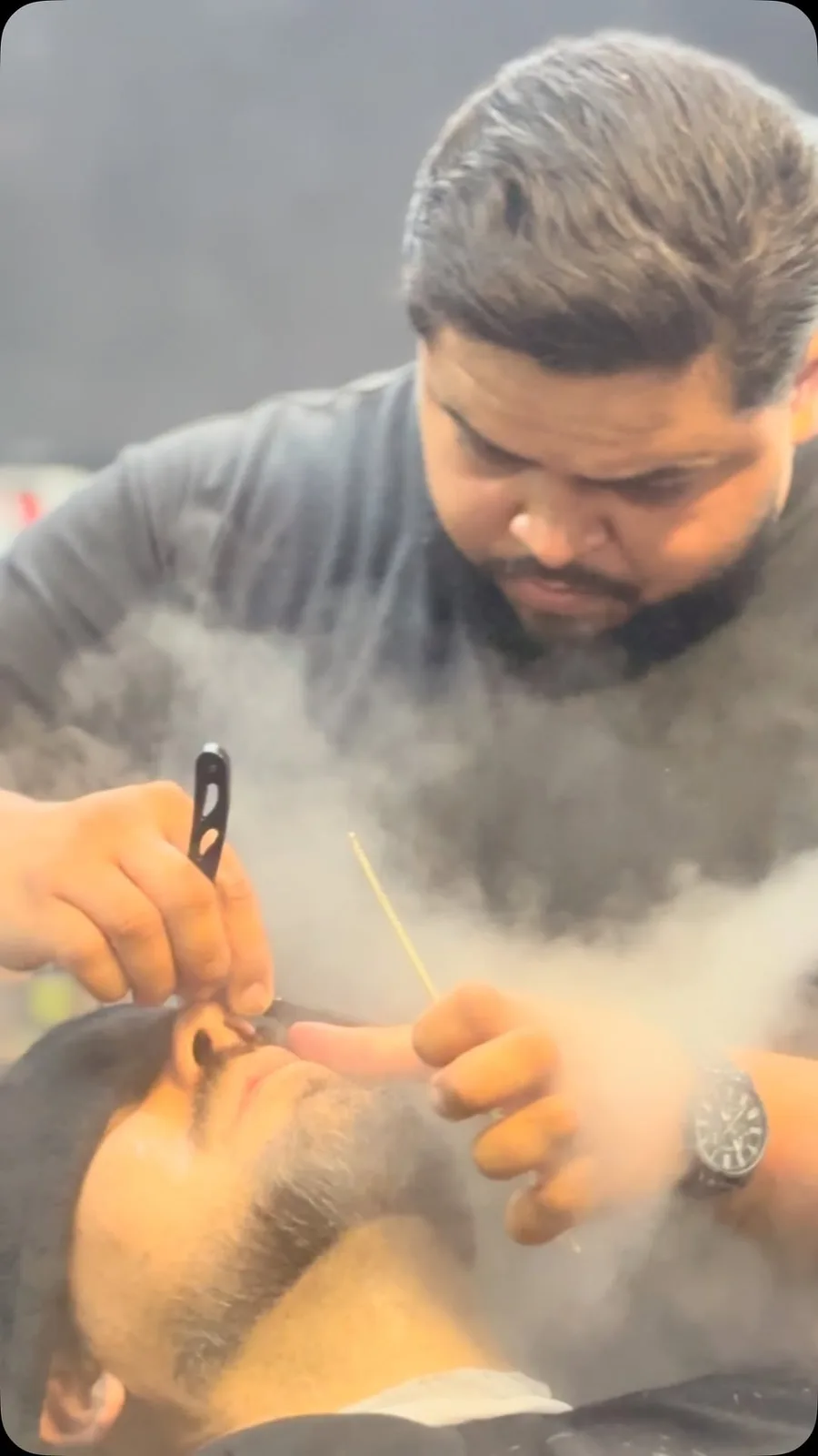 Barbeiro da The Barber's fazendo a barba de um cliente com navalha e toalha quente